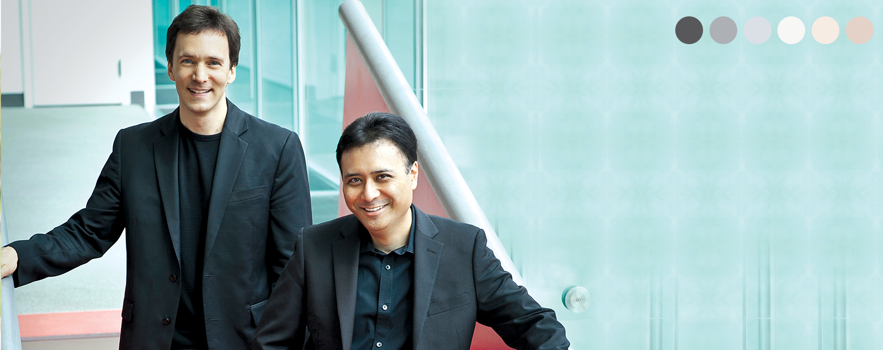 Two musicians standing on stairs smiling against a blue background.